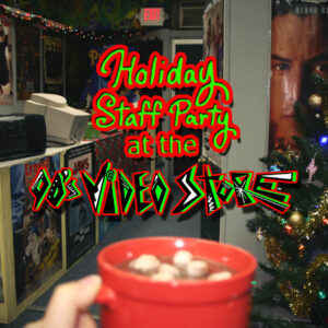 Holiday Staff Party at the 90s Video Store! A mug of hot chocolate overlooks a Video Store with a Keanu Reeves Speed poster and Christmas Tree next to it.